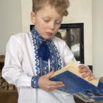 Хлопчик читає книжку у дитячій вишиванці з синім орнаментом, льон